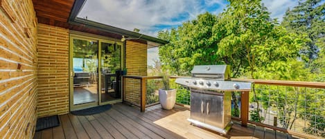 Une terrasse en bois avec un barbecue et une porte vitrée donnant sur un espace extérieur.