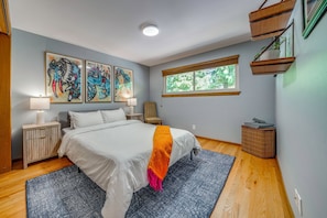 Un dormitorio con cama, mesitas de noche, una ventana, obras de arte y una pequeña mesita auxiliar.