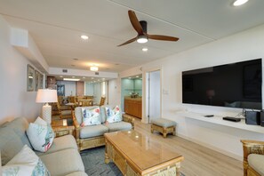 A spacious living room with a ceiling fan, a large flat-screen TV, and a dining area with wicker furniture. - Gulf-front SPI Condo: Suntide III - Unit 1009 (South Padre Island)