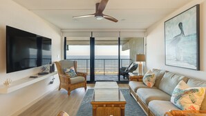Ein großzügiges Wohnzimmer mit Flachbildfernseher, bequemen Sitzgelegenheiten, Deckenventilator und Meerblick.