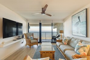 Ein großzügiges Wohnzimmer mit Flachbildfernseher, bequemen Sitzgelegenheiten, Deckenventilator und Meerblick.