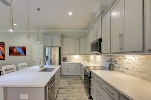 A modern kitchen with white cabinetry, a marble island, stainless steel appliances, and pendant lighting. - Gateway to Wec! Twin Ocala Townhomes (Ocala)