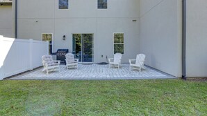A patio with white chairs and a grill, a white fence, and a building with a flat roof and large windows. - Twin Ocala Townhomes! 1 Mi to WEC (Ocala)