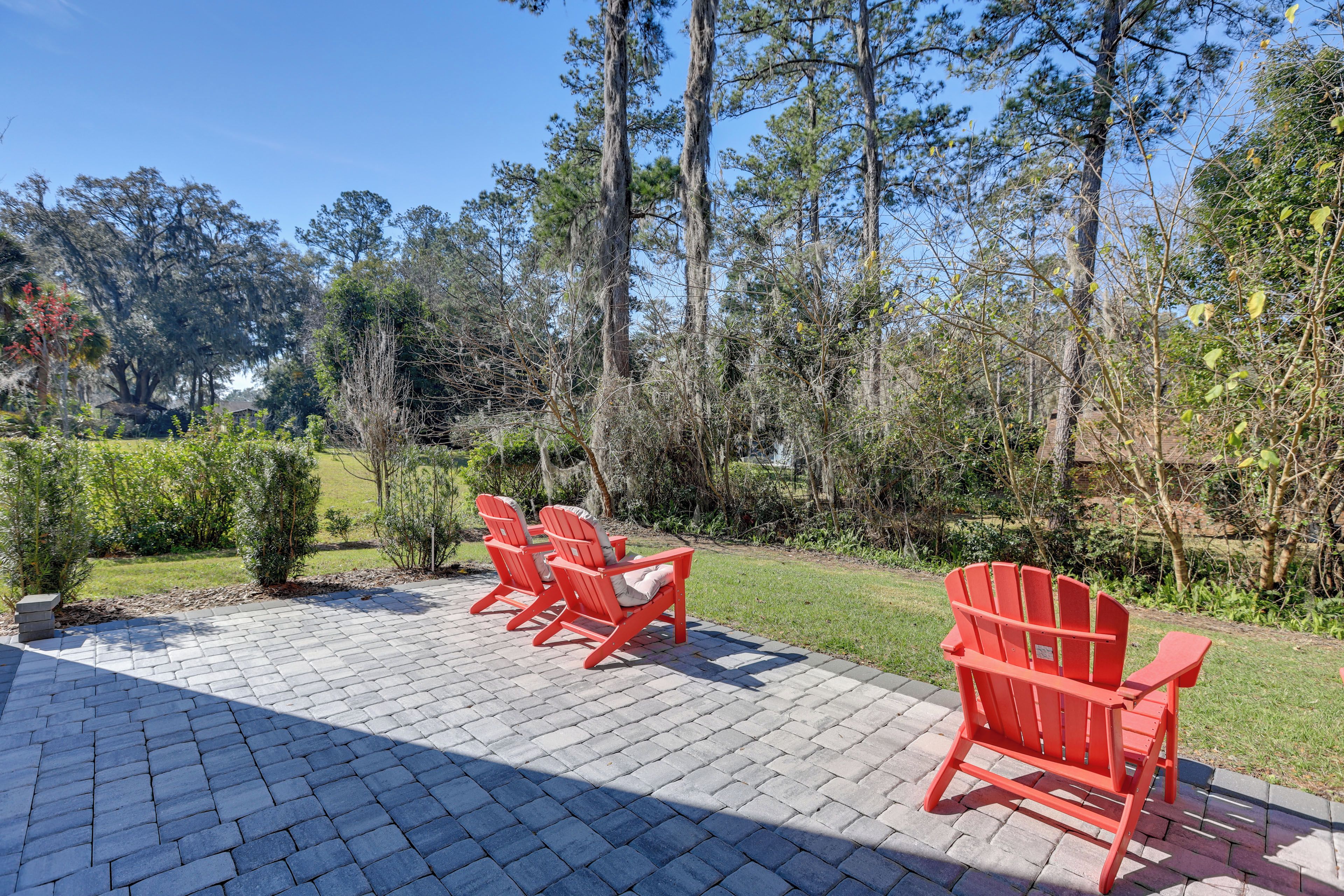 A paved patio with red Adirondack chairs and a view of a wooded area.