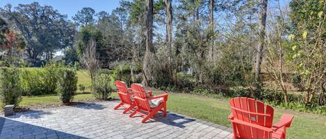A paved patio with red Adirondack chairs and a view of a wooded area.