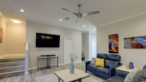 A modern living room with a flat-screen TV, a ceiling fan, and a large window. - Twin Ocala Townhomes! 1 Mi to WEC (Ocala)