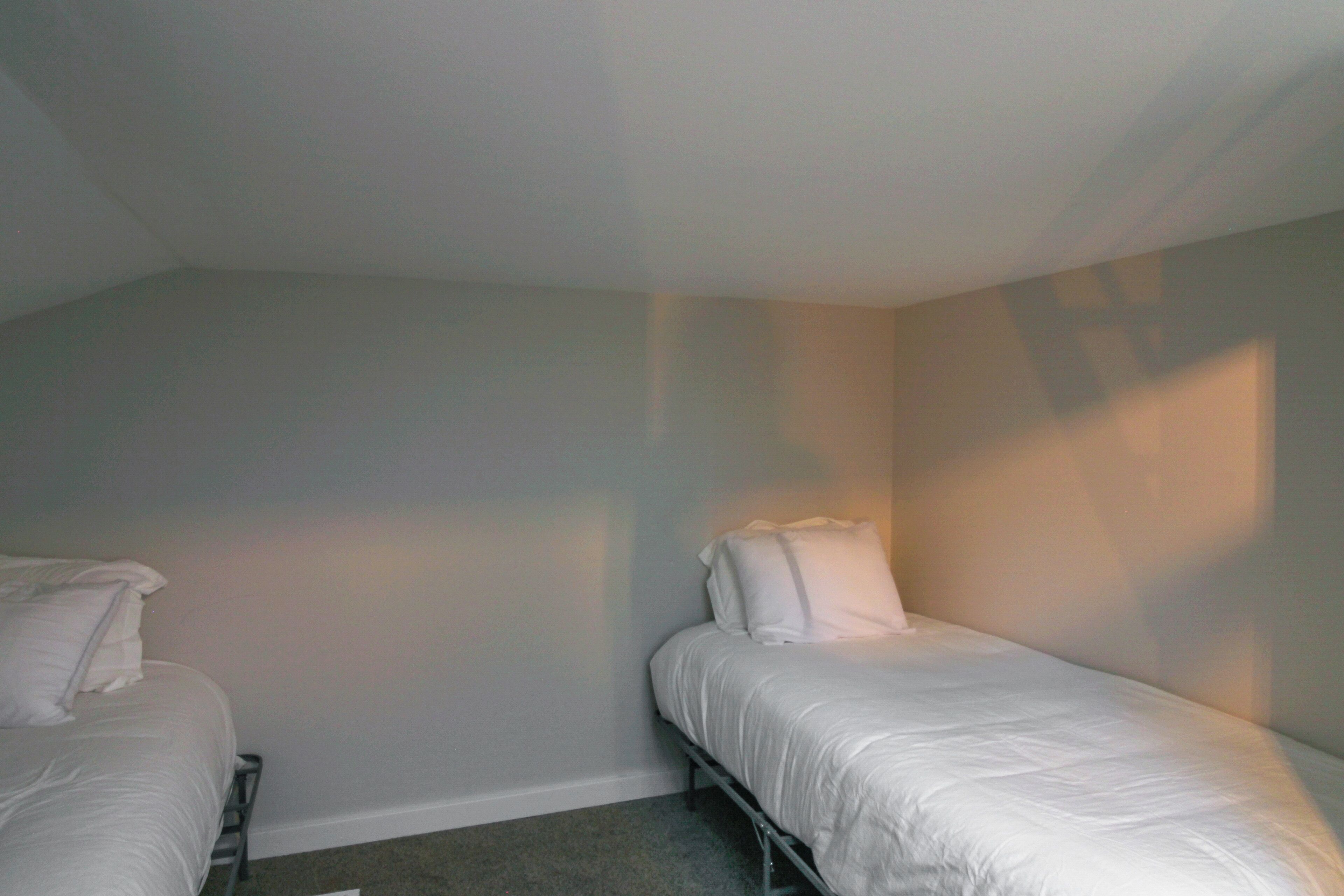 A small, dimly lit room with two single beds and a plain wall.