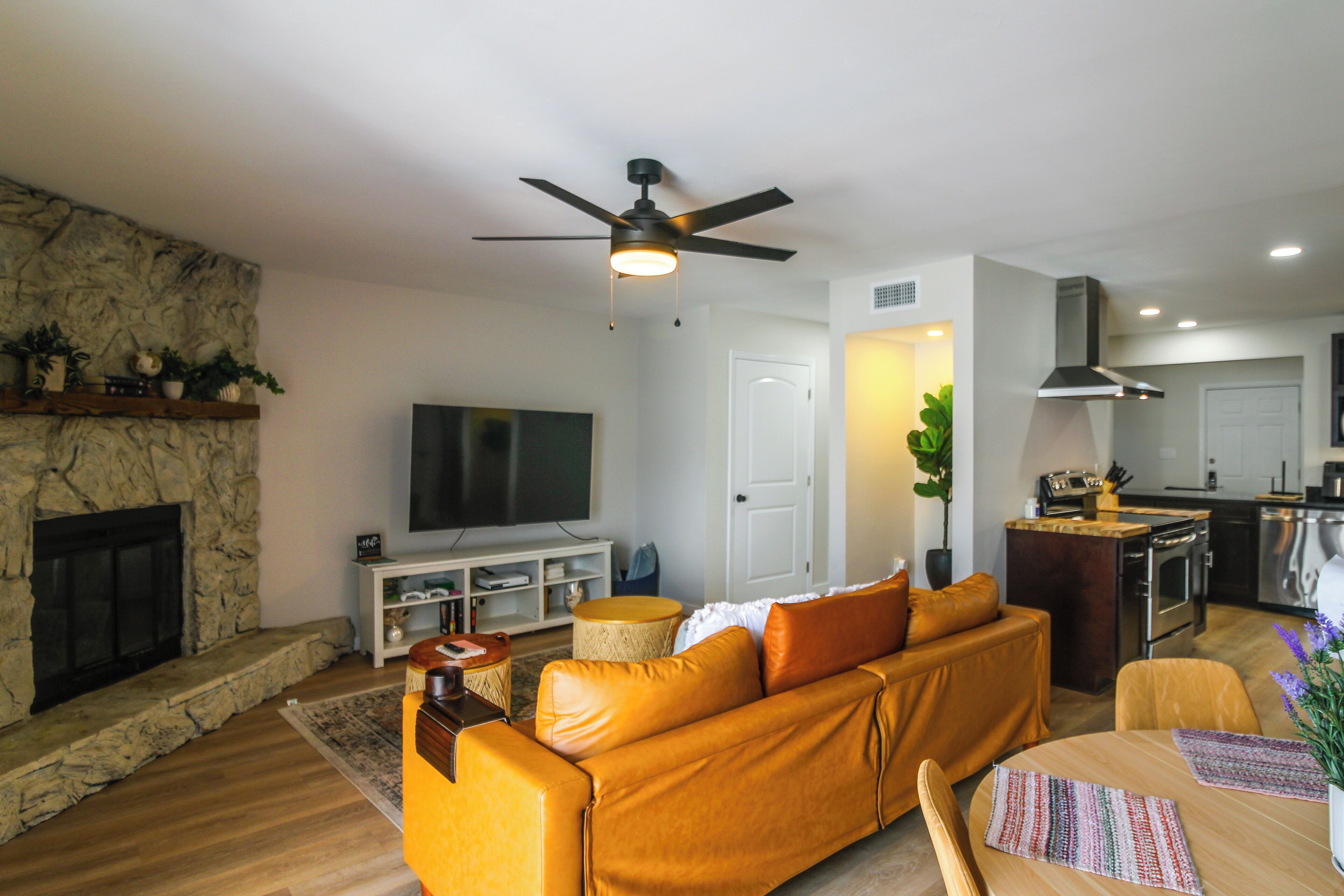 A modern living room with a stone fireplace, a sofa, a television, and a kitchen area.