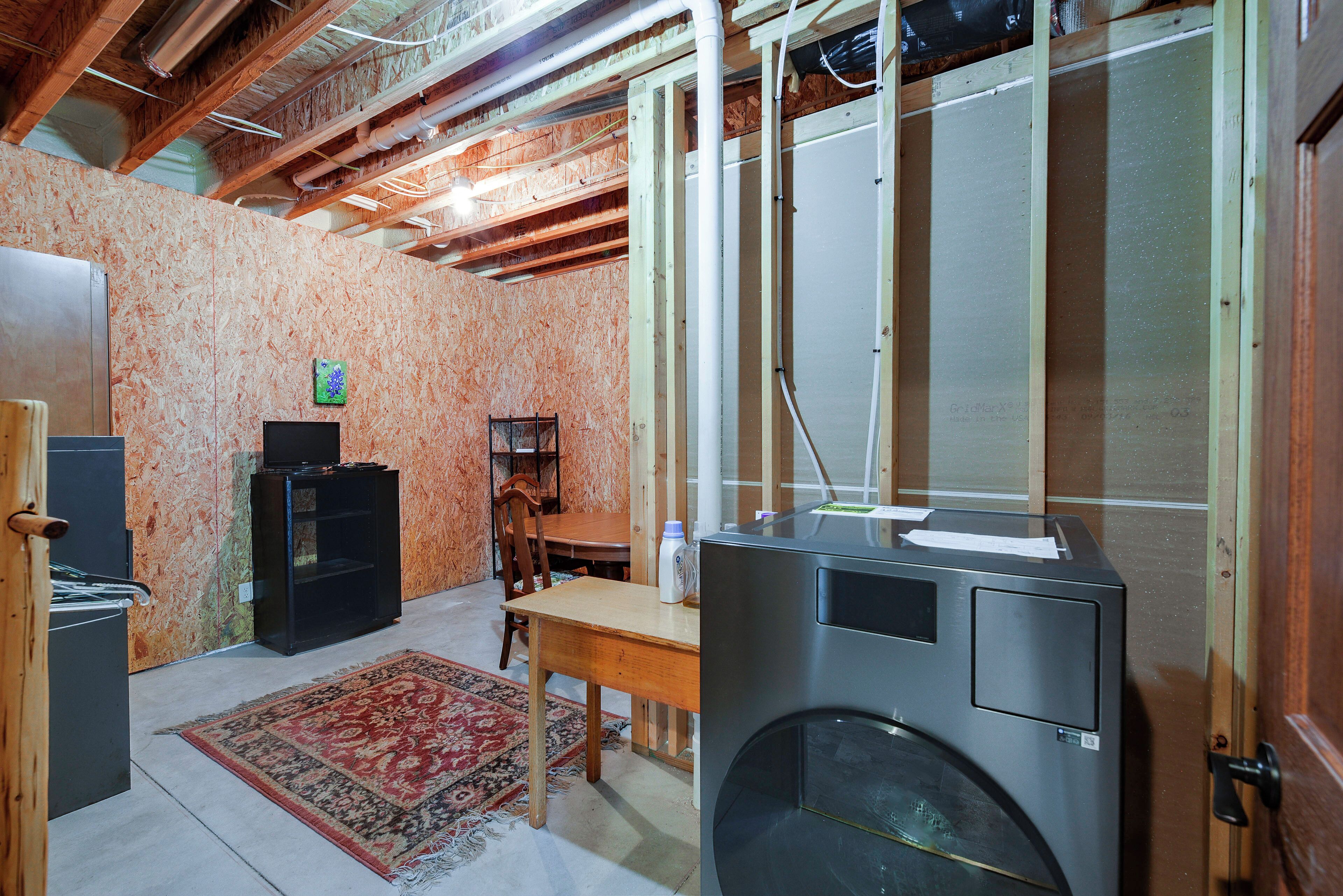 Een kamer met een grote wasmachine, een houten tafel, een stoel en een televisie op een standaard.
