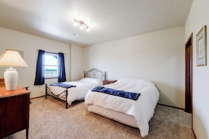 A bedroom with two single beds, a nightstand, a lamp, and a window with curtains.