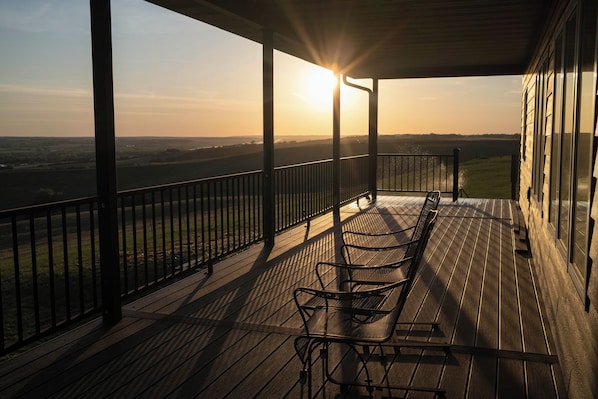 A wooden deck with a metal railing, a bench, and a view of the landscape.
