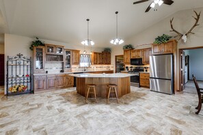 A spacious kitchen with a central island, wooden cabinets, stainless steel appliances, and a ceiling fan.