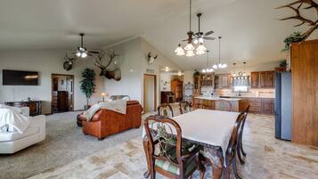 A spacious living area with a fireplace, a dining table with chairs, and a kitchen in the background.