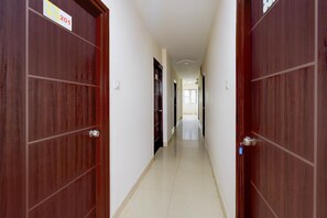 A corridor with wooden doors, a tiled floor, and a light-colored wall. - Hotel O Netaji Park Hyderabad (Hyderabad)