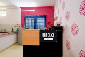 A reception desk with a sign that reads 'HOTEL OYO-Serviced' in a room with pink walls, a blue curtain, and patterned wallpaper. - Hotel O Netaji Park Hyderabad (Hyderabad)