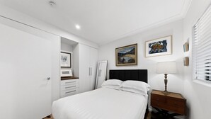 A bedroom with a bed, a dresser, a nightstand, a lamp, and two framed pictures on the wall. - Balcony 2-bed Apartment in Ashgrove (Brisbane)