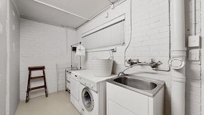 A laundry room with a washing machine, a sink, and a wooden stool. - Balcony 2-bed Apartment in Ashgrove (Brisbane)