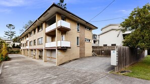 A multi-story residential building with a brick facade, a gated driveway, and a fenced yard. - Balcony 2-bed Apartment in Ashgrove (Brisbane)