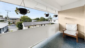 A balcony with hanging planters, a white chair, and a view of neighboring houses. - Balcony 2-bed Apartment in Ashgrove (Brisbane)