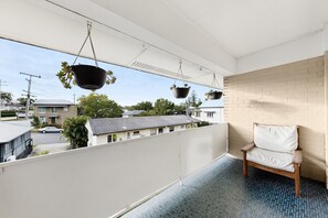 Ein Balkon mit hängenden Pflanzgefäßen, einem weißen Stuhl und Blick auf Nachbarhäuser.