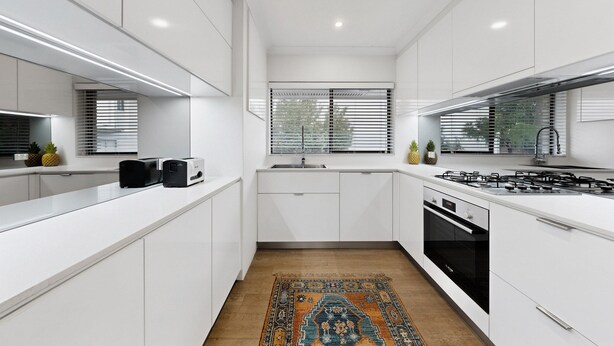 A modern kitchen with white cabinetry, a gas stove, a built-in oven, and a window with blinds. - Balcony 2-bed Apartment in Ashgrove (Brisbane)
