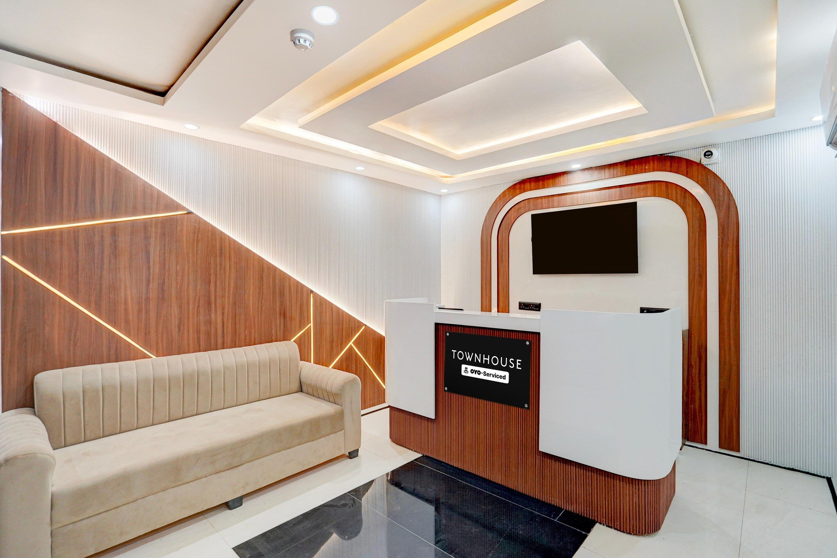 A reception area with a modern design, including a wooden accent wall, a beige sofa, and a reception desk with a sign that reads 'TOWNHOUSE OYO-Serviced.'