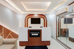 A reception area with a modern design, including a reception desk, a flat-screen TV, and a glass partition. - Classic RR Grand (Varanasi)