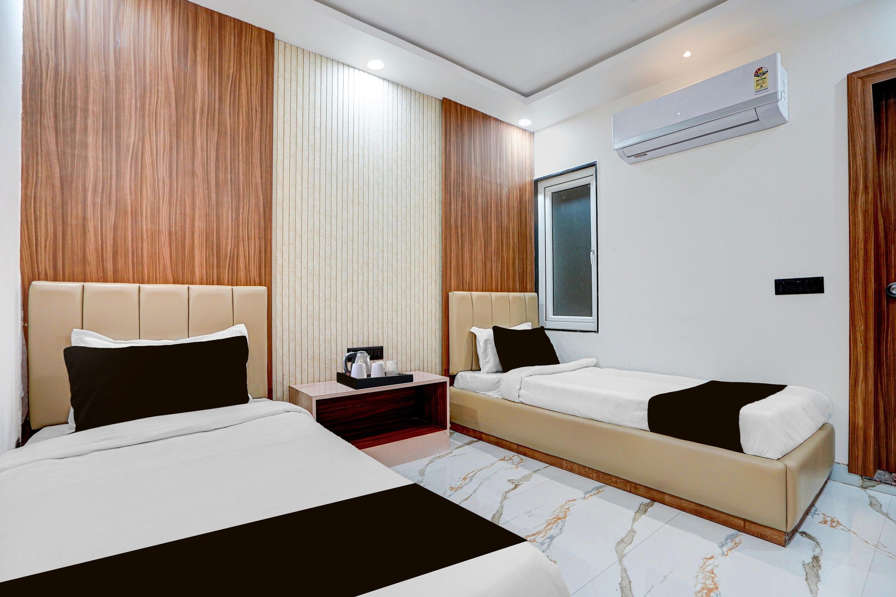 A hotel room with two beds, a bedside table, an air conditioning unit, and a window.