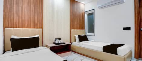 A hotel room with two beds, a bedside table, an air conditioning unit, and a window.