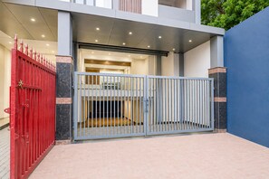 A gated entrance with a red gate and a grey gate, leading to a building with a tiled floor and a balcony. - Classic RR Grand (Varanasi)