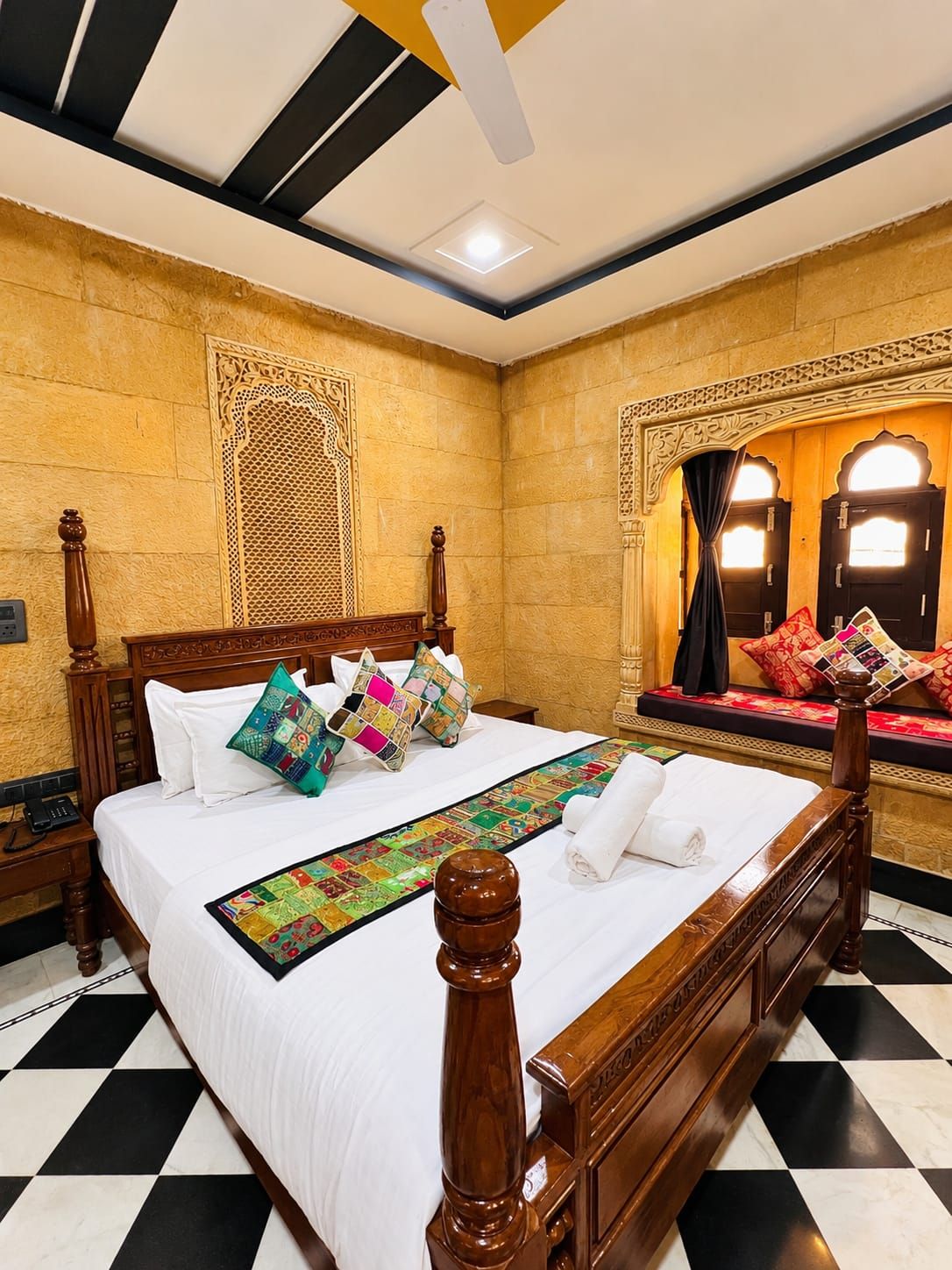 Habitación de hotel con una cama grande, un cabecero decorativo, un corredor de cama estampado y vistas al exterior a través de una ventana con cortinas.