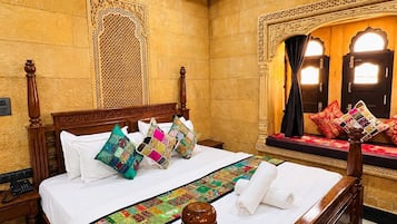 Habitación de hotel con una cama grande, un cabecero decorativo, un corredor de cama estampado y vistas al exterior a través de una ventana con cortinas.