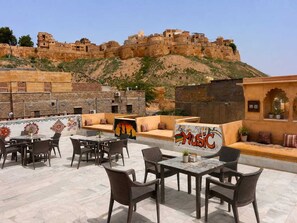 Un espacio al aire libre con muros de piedra, un mural y vista a una fortaleza histórica.