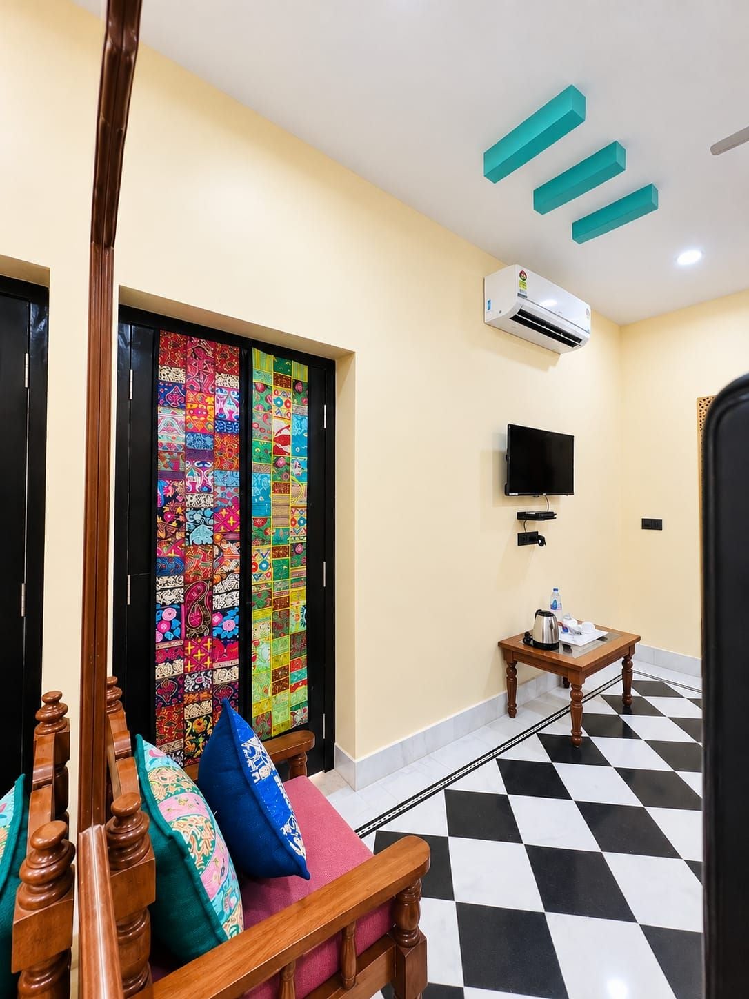Una habitación de hotel con piso a cuadros, un televisor, un equipo de aire acondicionado y una puerta colorida.