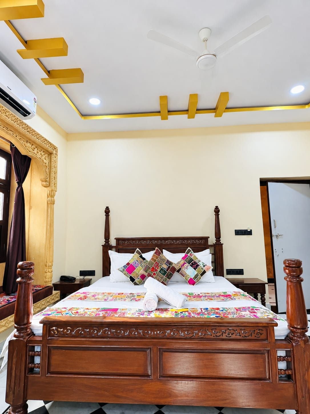 A hotel room with a wooden bed, a ceiling fan, and a decorative wall panel.