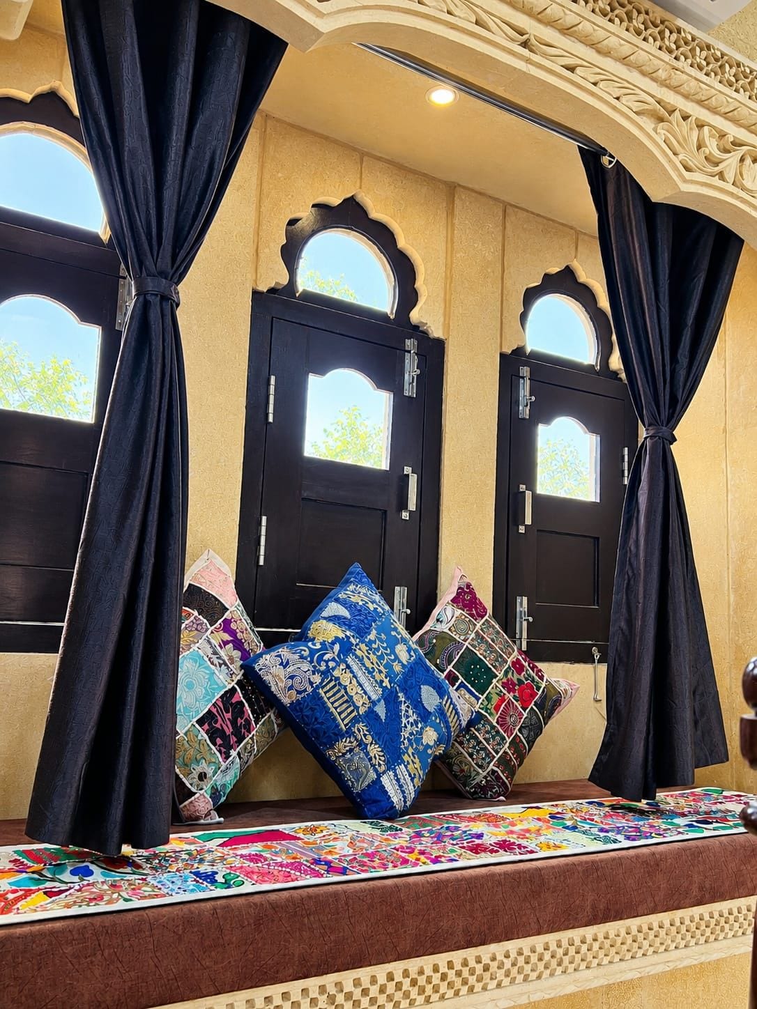 Una habitación con dos puertas negras, cada una con un ventanal pequeño, y un banco con cojines de colores.