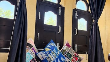 Una habitación con dos puertas negras, cada una con un ventanal pequeño, y un banco con cojines de colores.