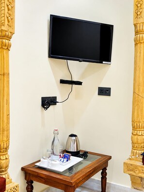 Una habitación con televisor montado, una mesa con cafetera, una botella y una taza.