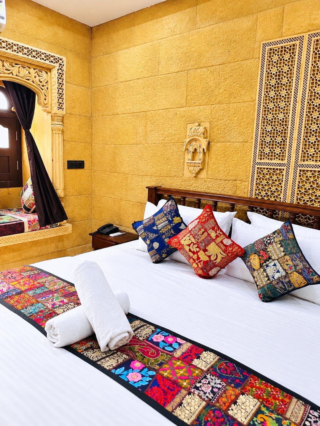 A hotel room with a bed, pillows, a wall-mounted light fixture, and a decorative wall panel.