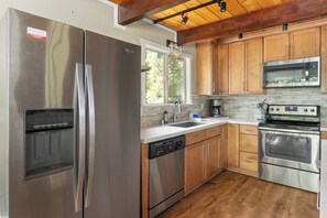 A modern kitchen with stainless steel appliances, wooden cabinets, and a large window. - Sophie's Den- BLS Rec access, sleeps 12 (Arnold)