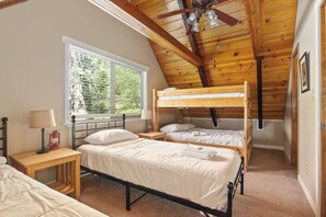 Une chambre avec deux lits superposés, une fenêtre avec des stores, une lampe et un ventilateur de plafond.