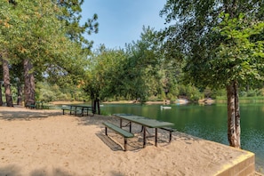 Une plage de sable avec des tables et des bancs pour pique-niquer, entourée d’arbres et bordée d’un lac paisible.