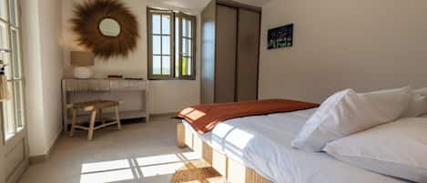 Un dormitorio con cama, mesita de noche, espejo, ventana y puerta.