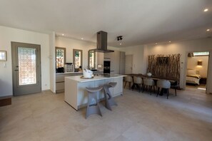 A modern kitchen with a central island, bar stools, and a dining area with chairs. - Luxury Charm Villa Heart of village, large swimming pool, large private garden (Grimaud)