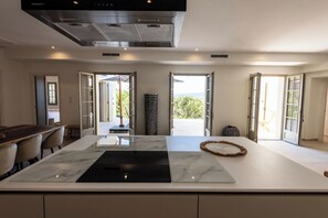 A modern kitchen with a marble countertop, a built-in stove, and a view of the outdoors. - Luxury Charm Villa Heart of village, large swimming pool, large private garden (Grimaud)
