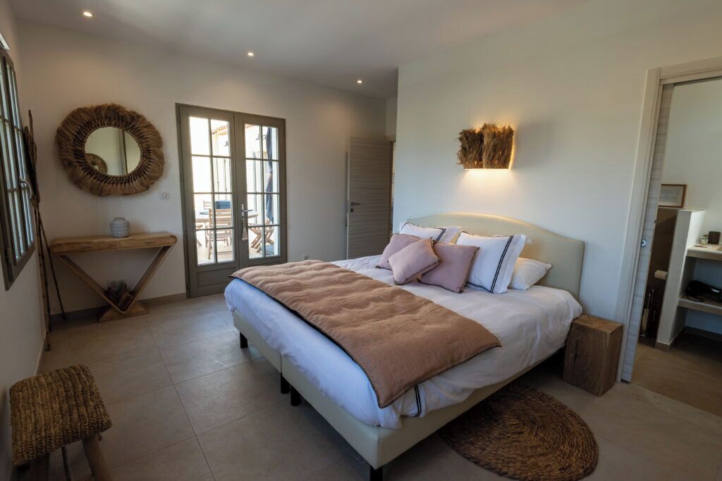 A bedroom with a bed, bedside tables, a mirror, and a view through a glass door.