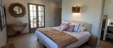 A bedroom with a bed, bedside tables, a mirror, and a view through a glass door.