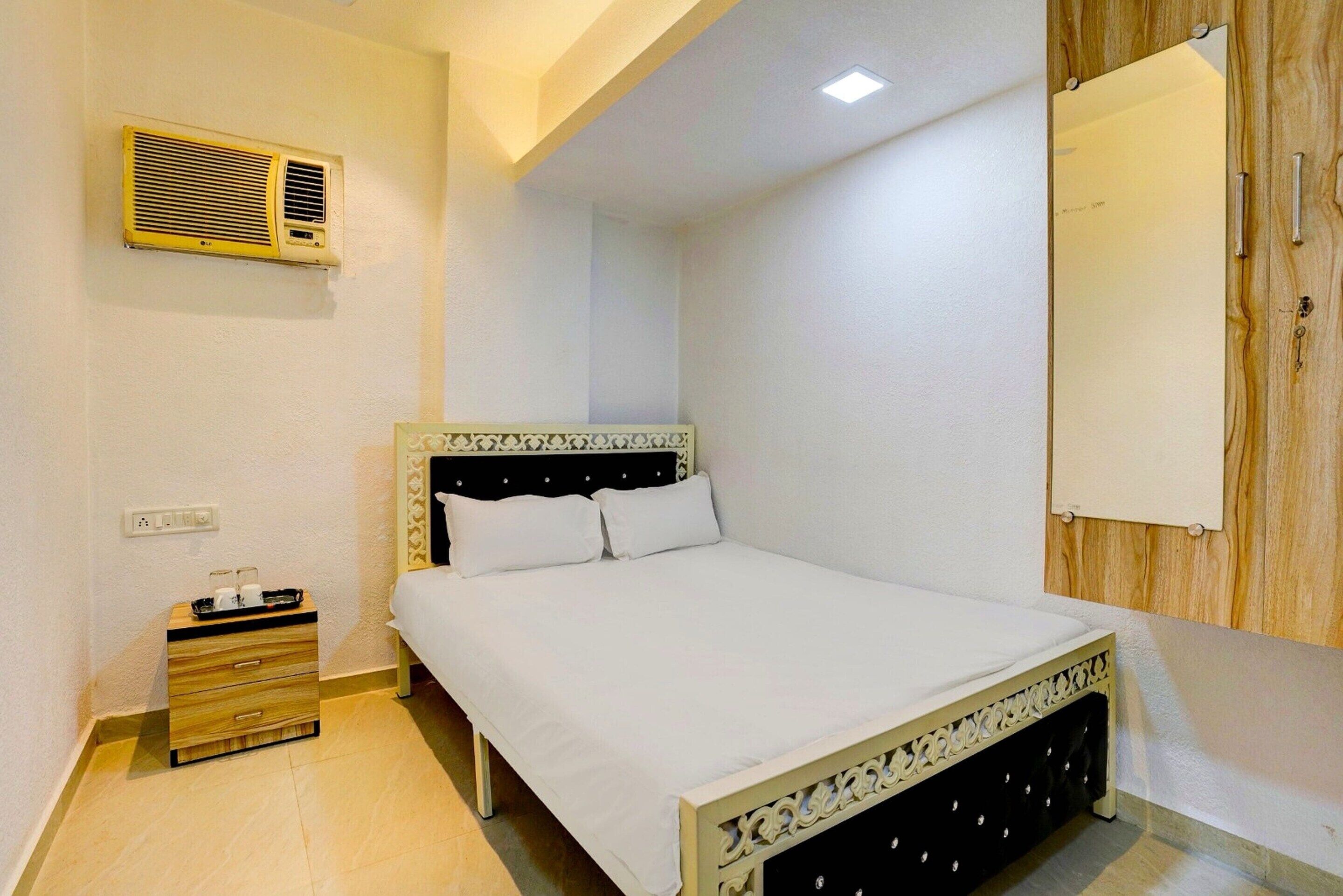 A bedroom with a bed, a bedside table, a drawer, a wall-mounted air conditioner, and a wooden panel wall.