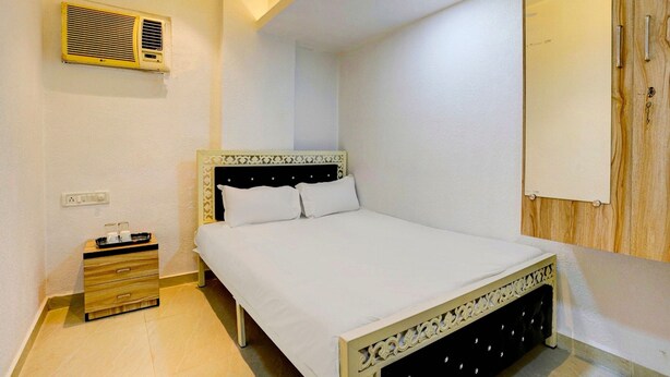 A bedroom with a bed, a bedside table, a drawer, a wall-mounted air conditioner, and a wooden panel wall. - Deluxe Room Santacruz Metro (Mumbai)