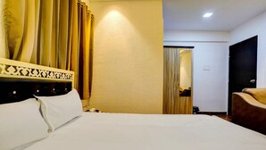 A hotel room with a bed, a chair, a wooden door, and a mirror. - Deluxe Room Santacruz Metro (Mumbai)
